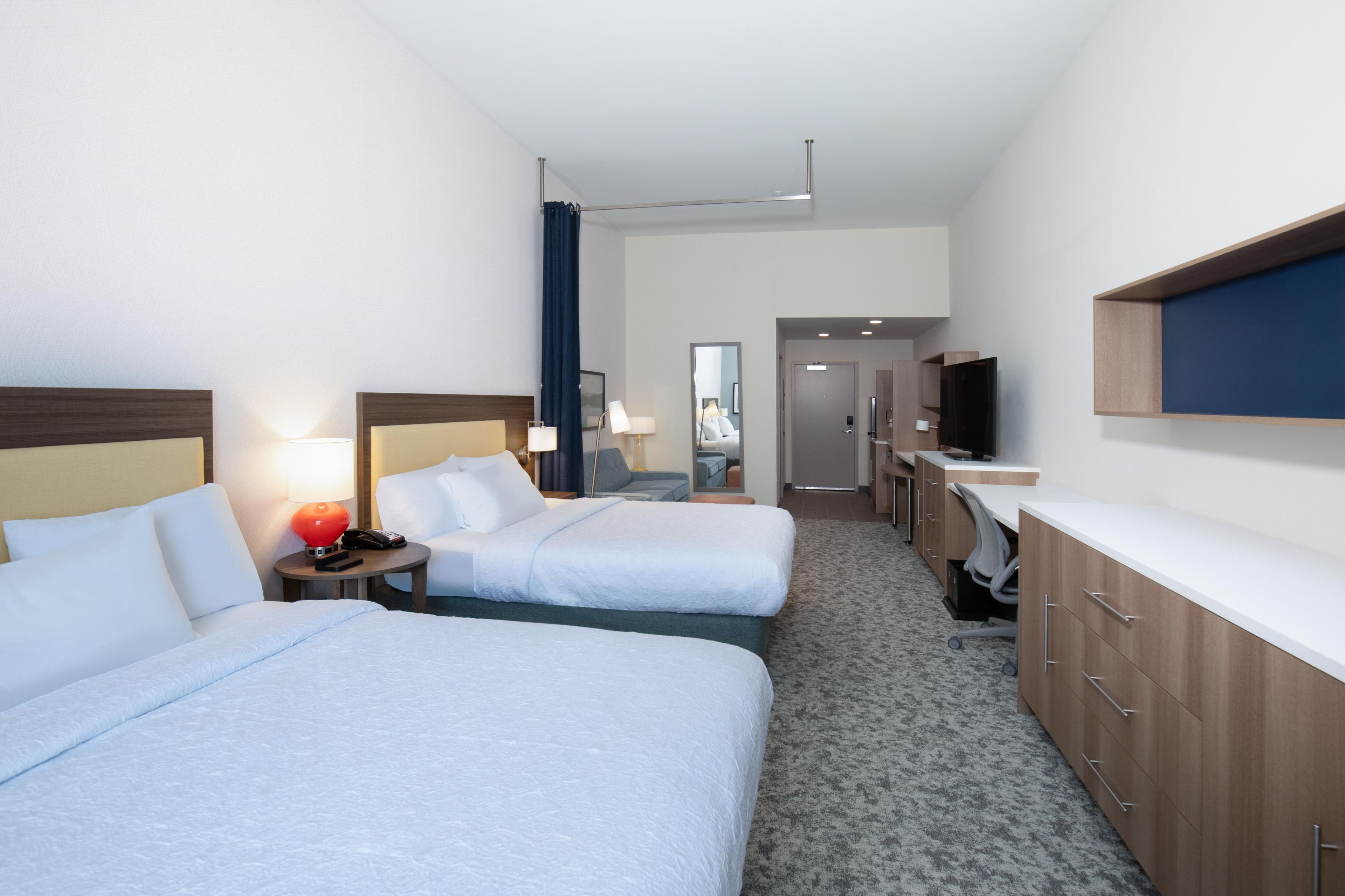 Una camera d'albergo con due letti, una scrivania, una TV e un bagno.