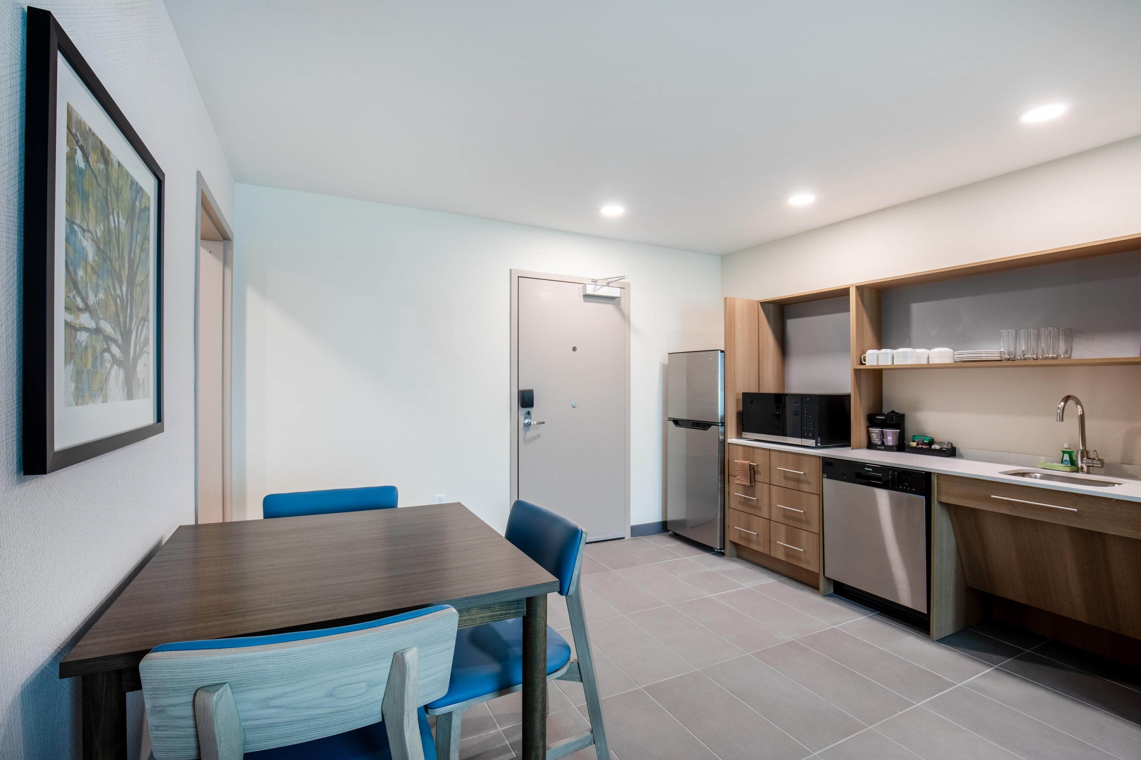 A modern kitchen with a dining area, featuring a refrigerator, microwave, and wooden cabinets.