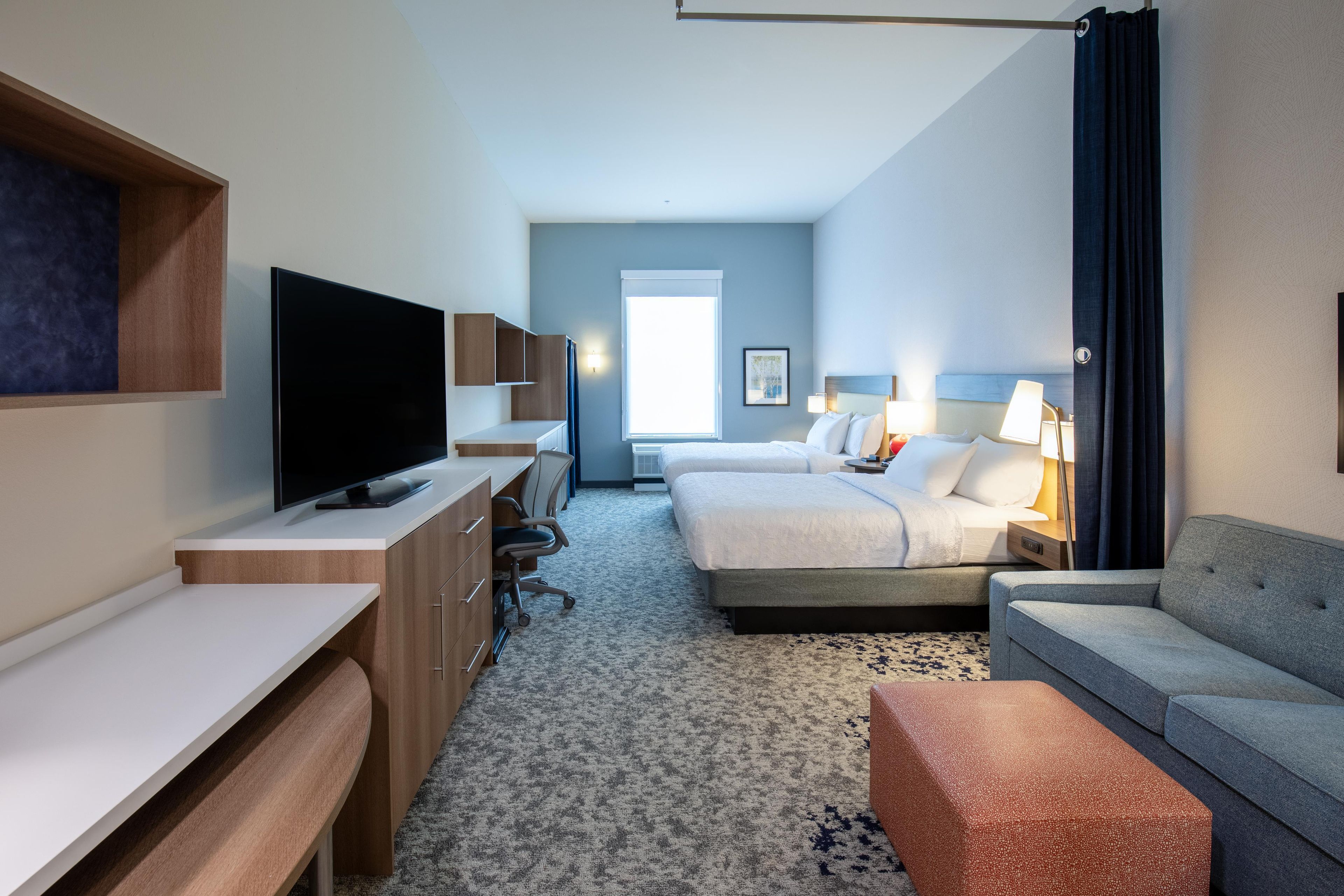 A hotel room with a flat-screen TV, a desk, a bed, a sofa, and a small table.
