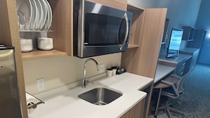 Een moderne keuken met een ingebouwde magnetron, een roestvrijstalen spoelbak en houten keukenkastjes.