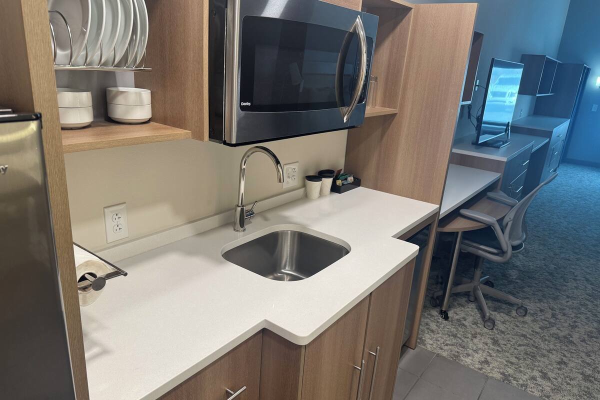 Een moderne keuken met een ingebouwde magnetron, een roestvrijstalen spoelbak en houten keukenkastjes.