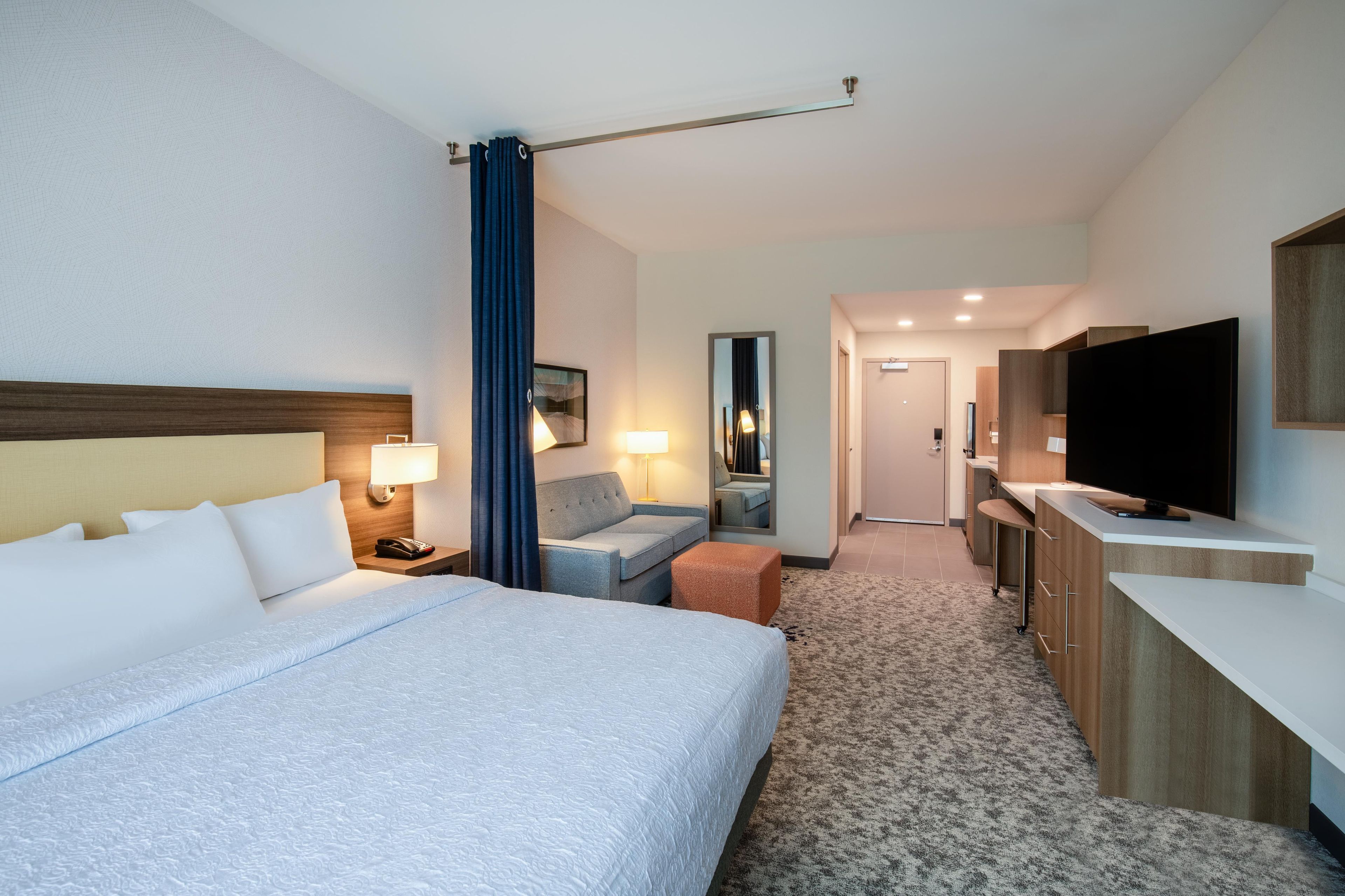Habitación de hotel con una cama grande, un escritorio, un televisor y un baño visible a través de una puerta abierta.