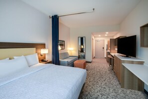 Een hotelkamer met een groot bed, een bureau, een televisie en een badkamer die door een open deur zichtbaar is.