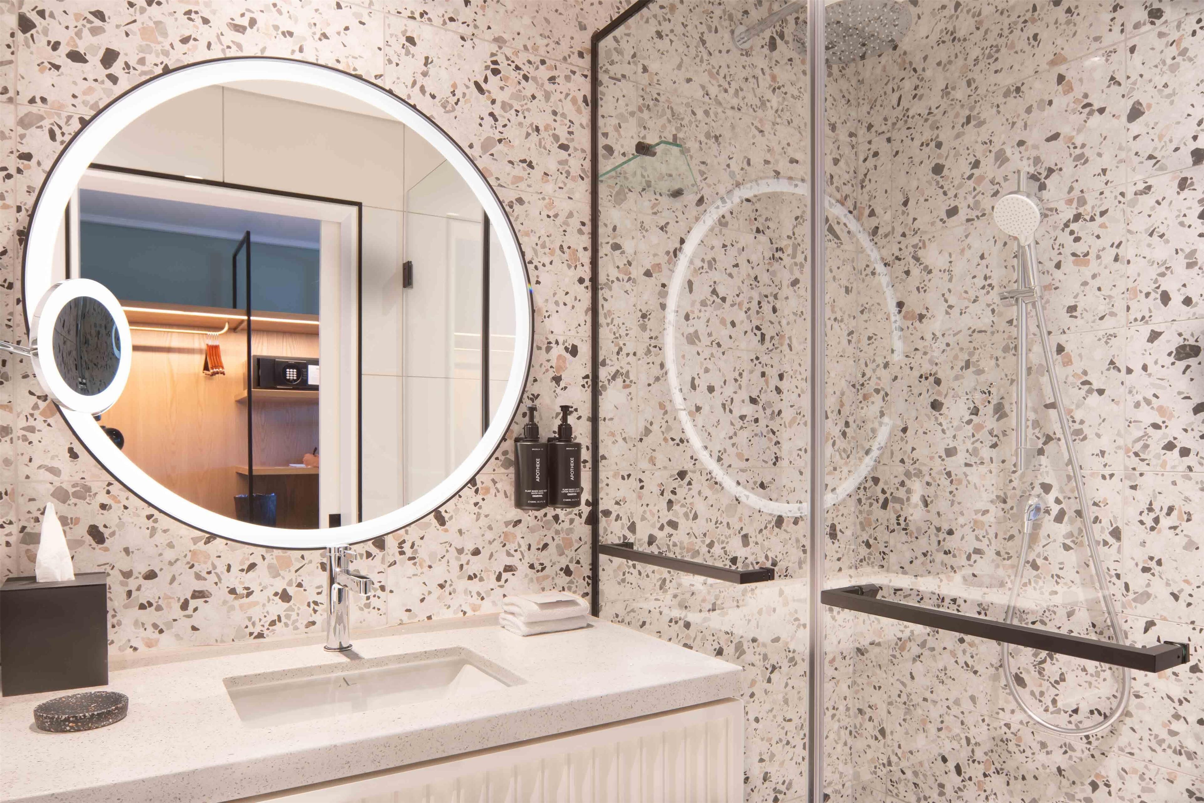A modern bathroom with a round mirror, a sink, and a shower area.