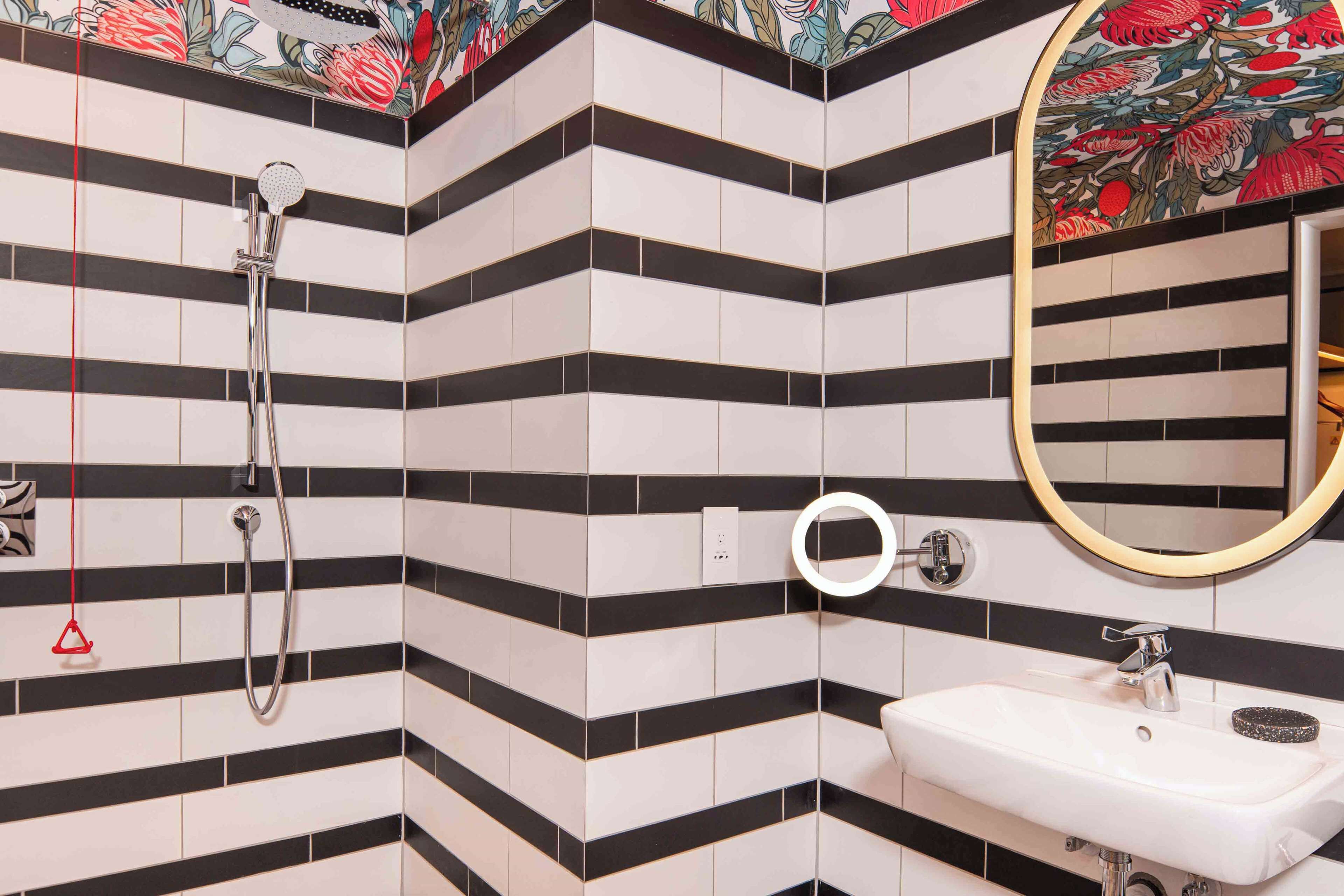 A bathroom with black and white striped tiles, a white sink, a mirror with a floral frame, and a showerhead.