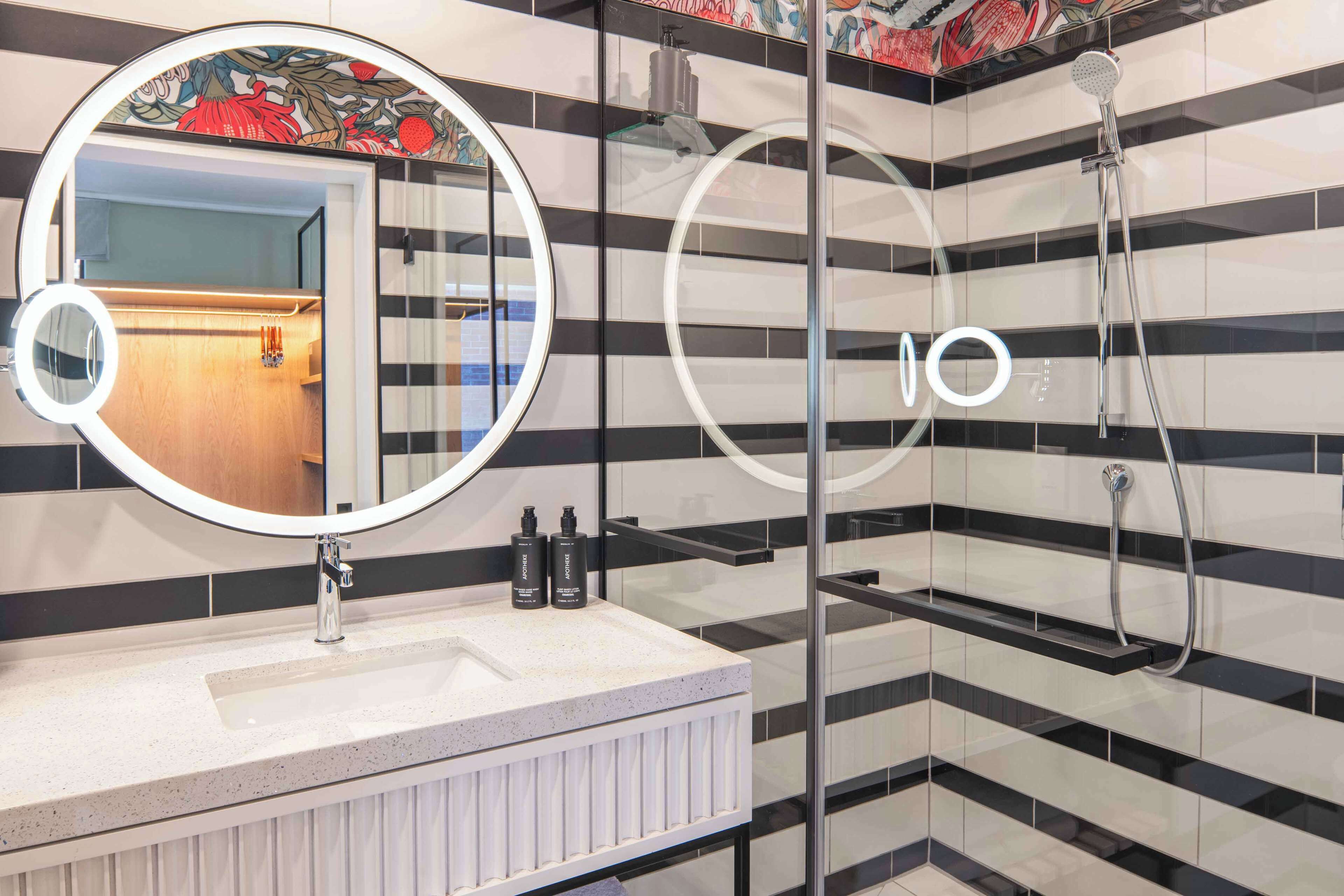A modern bathroom with a large mirror, a shower, and a vanity with a sink.