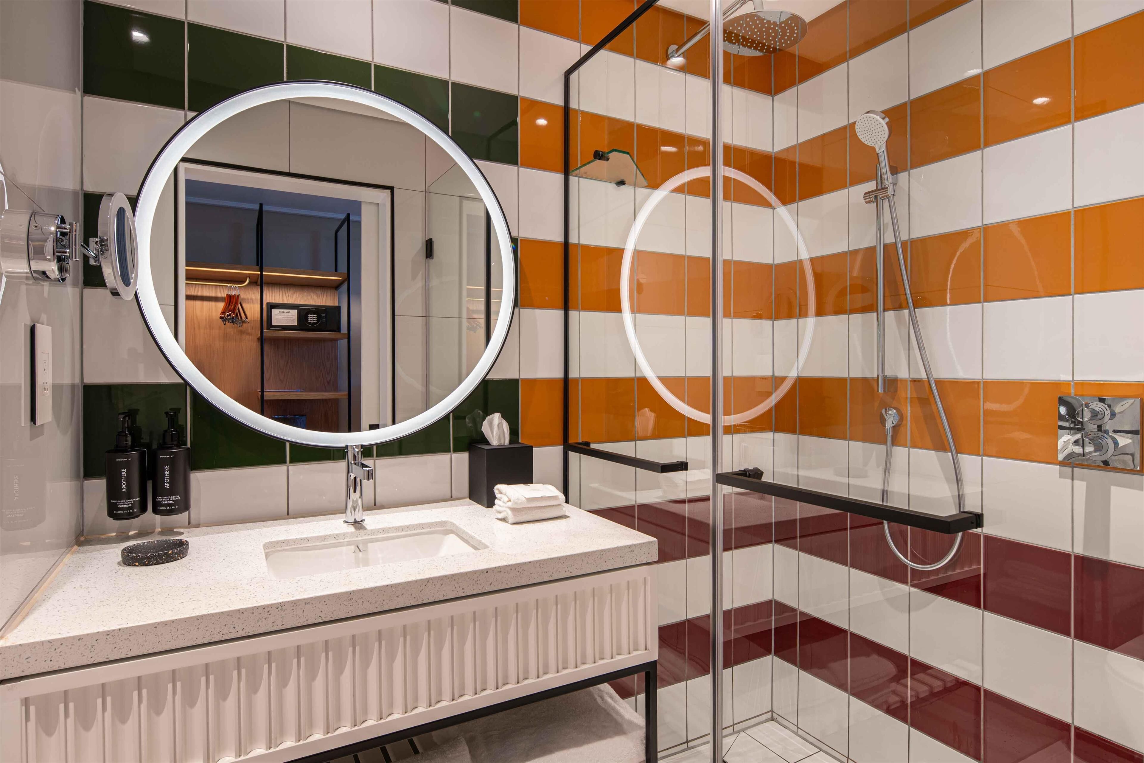 Un baño moderno con un espejo grande, ducha con mampara de vidrio y tocador con lavabo y toallero.