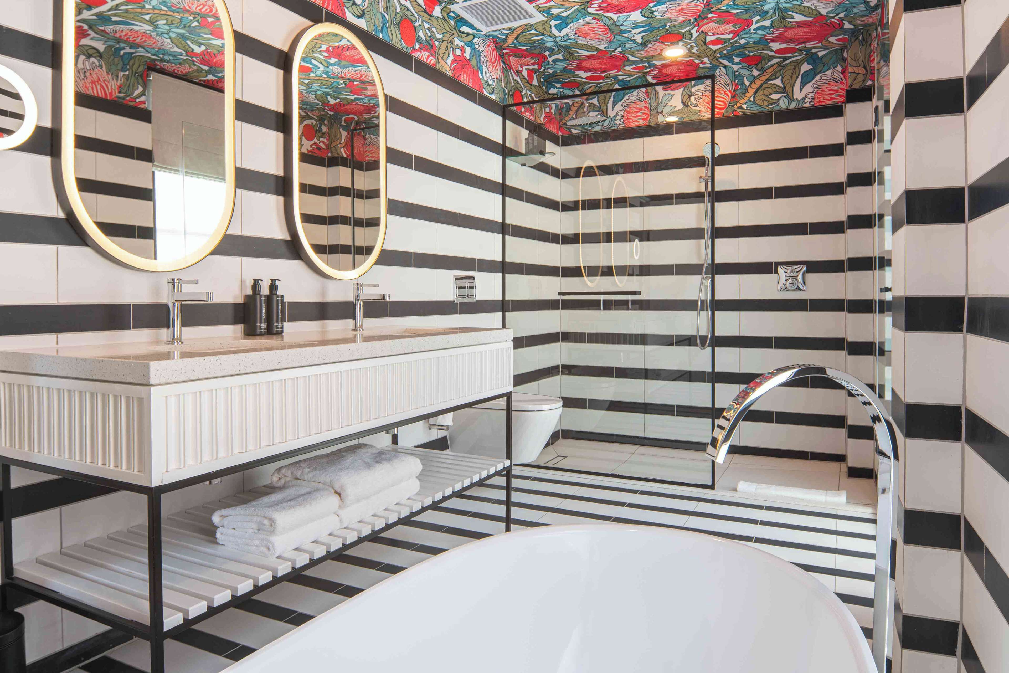 A modern bathroom with a striped tile design, a white vanity with a mirror, a bathtub, and a shower area.