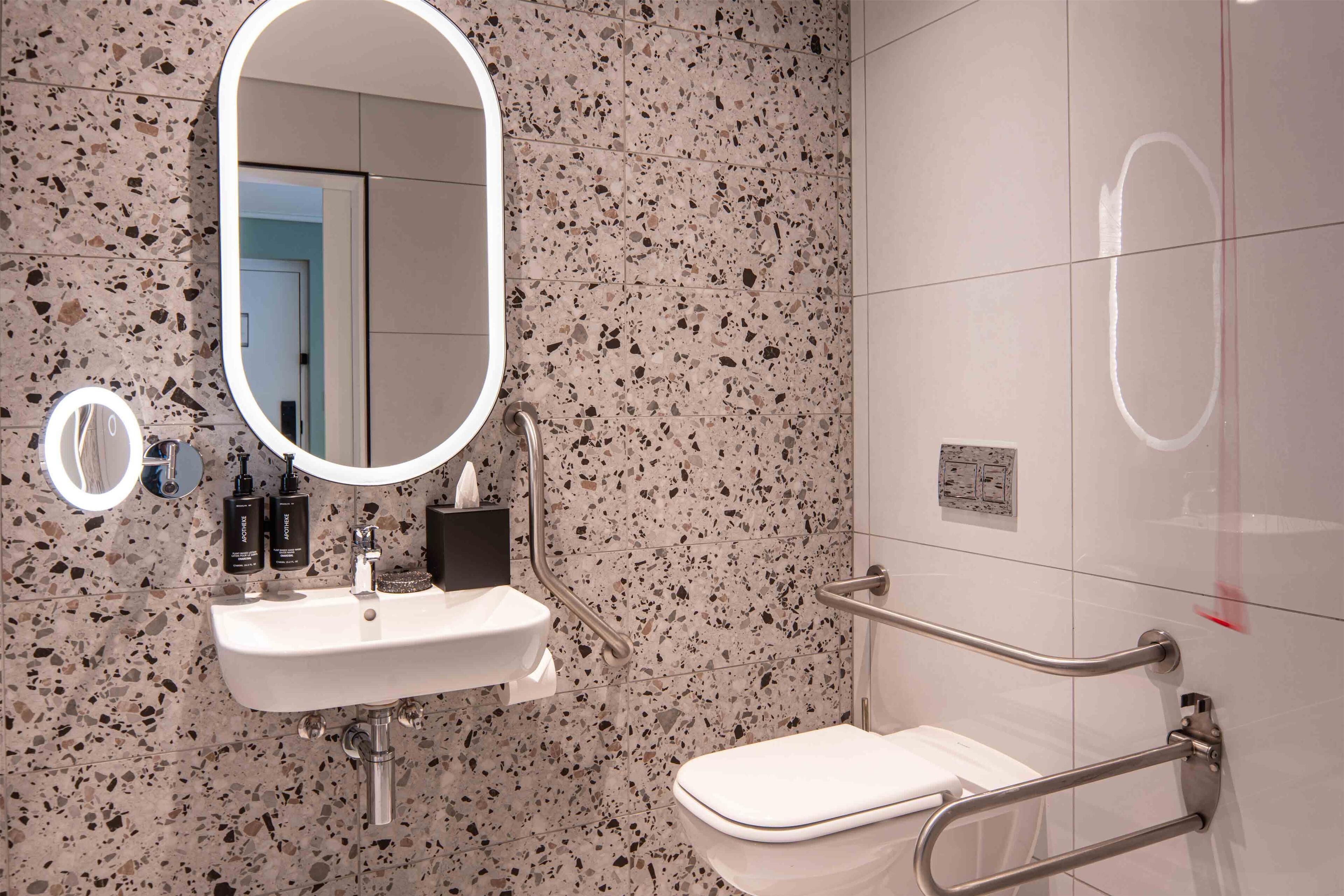 A bathroom with a white sink, mirror, and handrails.