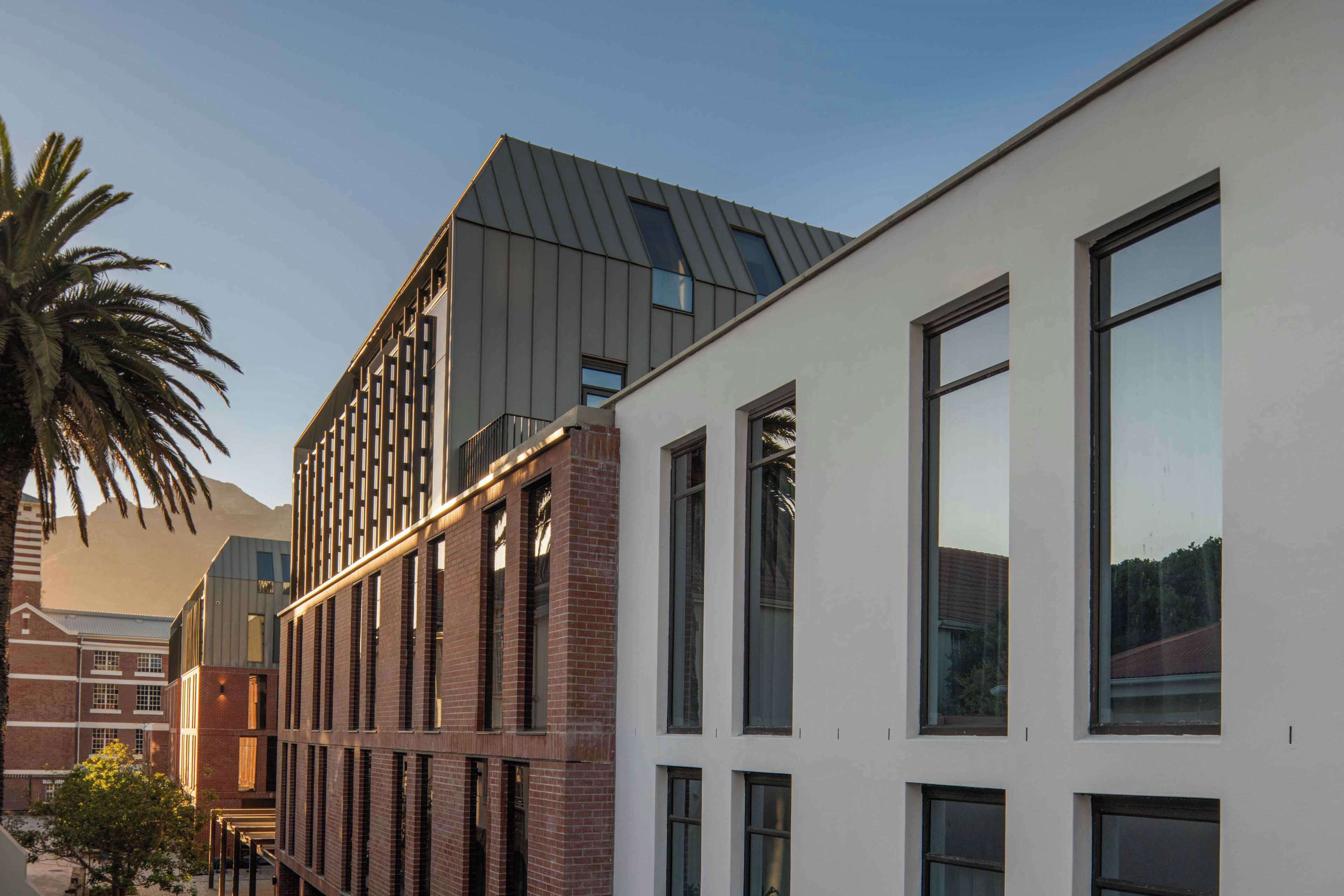 A modern building with a mix of brick and white facades, large windows, and a sloped roof.