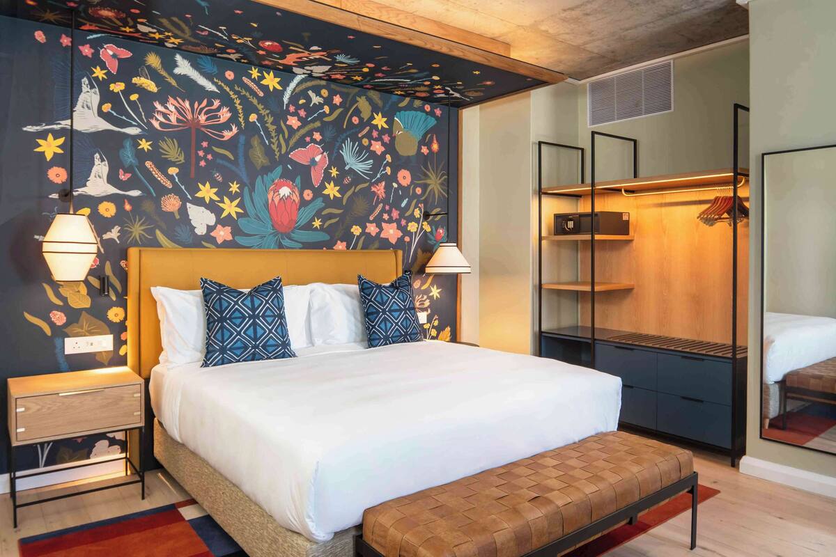 Habitación de hotel moderna con una cama grande, un banco, un armario y un espejo.