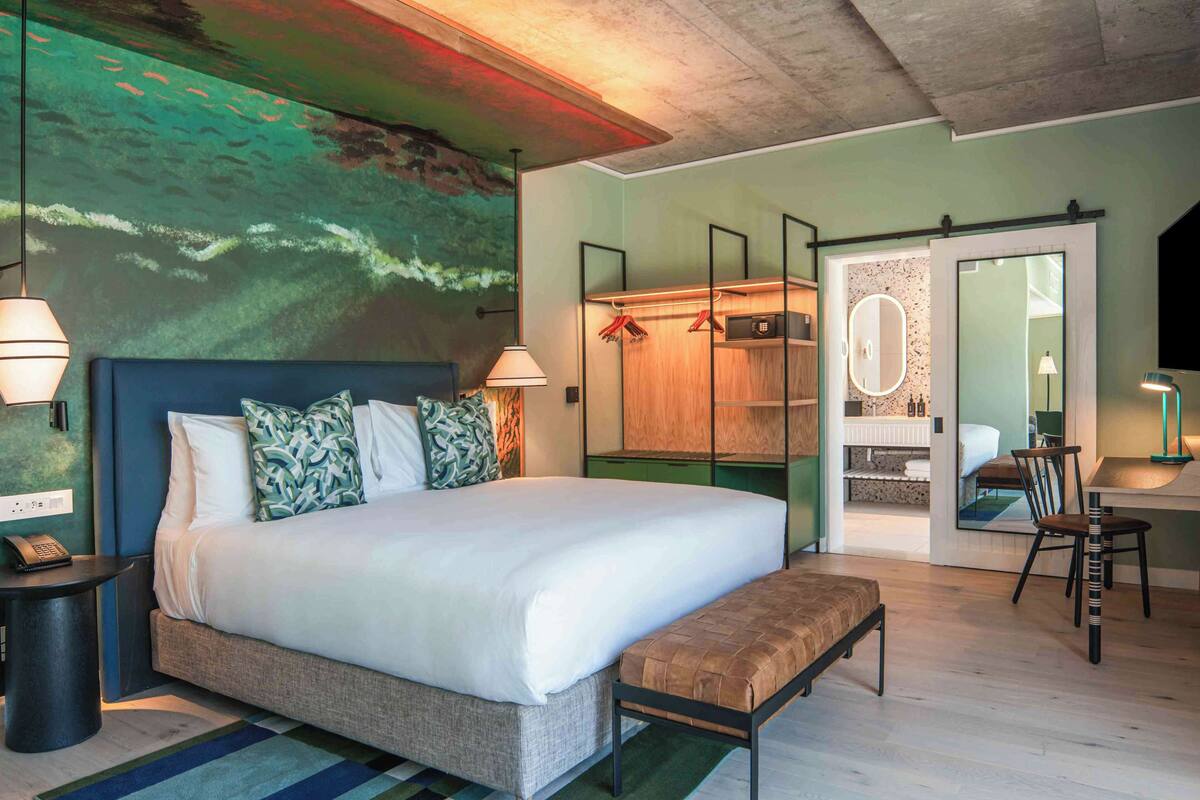 Una habitación de hotel moderna con una cama grande, un banco, un escritorio y un armario.