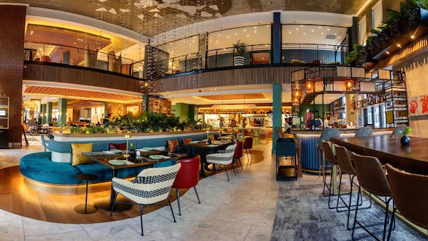 Un espacio interior de varios niveles con una zona de estar central, varias mesas de comedor y una escalera que conecta los niveles.