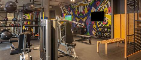 A gym with exercise equipment, a TV, and a colorful mural.