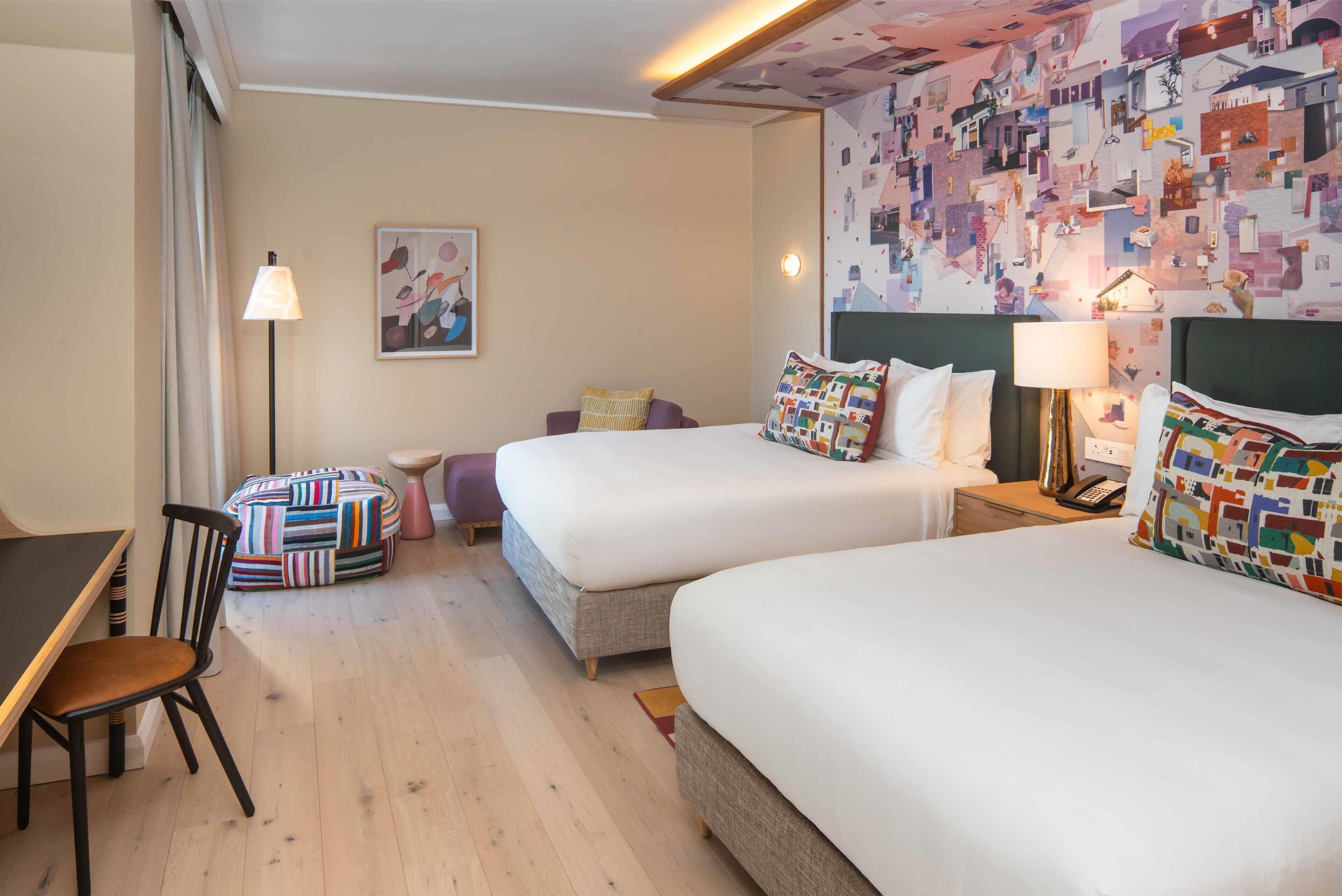 Une chambre d’hôtel avec deux lits, un bureau, une chaise et une décoration murale colorée.