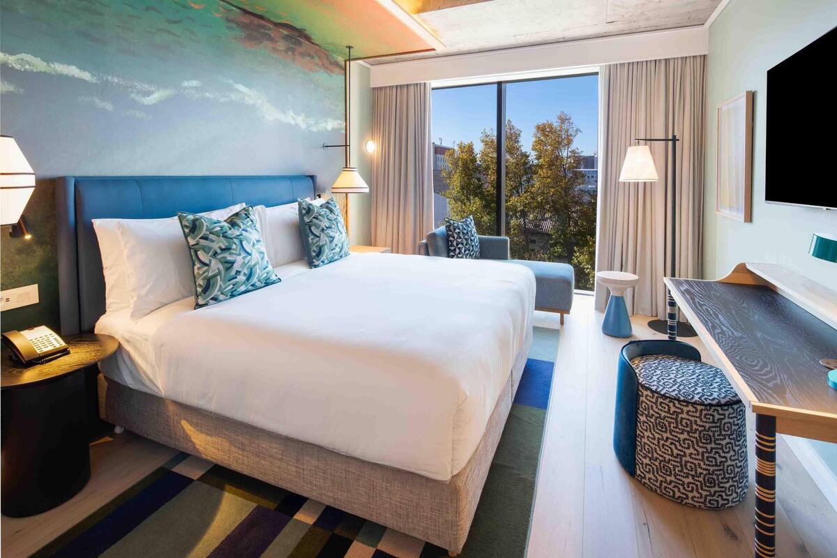 Habitación de hotel con una cama grande, un escritorio, una silla, un teléfono y un televisor.