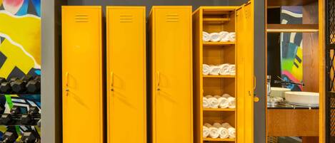 A set of yellow lockers with towels inside, a clock on the wall, and a colorful abstract painting.