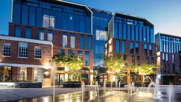 A modern building with a brick facade and large windows, a courtyard with a fountain, and outdoor seating.