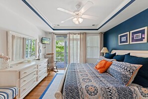A bedroom with a bed, a dresser, a chair, a ceiling fan, and a television.