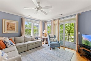 Ein Wohnzimmer mit einer Couch, einem Sessel, einem Fernseher und einem Deckenventilator.