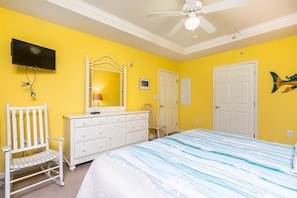 A bedroom with a bed, a dresser, a chair, a television, and a ceiling fan.
