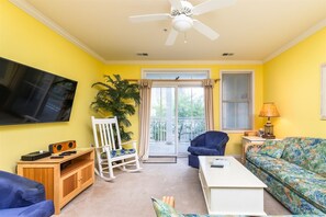 A living room with a television, a ceiling fan, a sofa, a coffee table, a chair, and a plant.