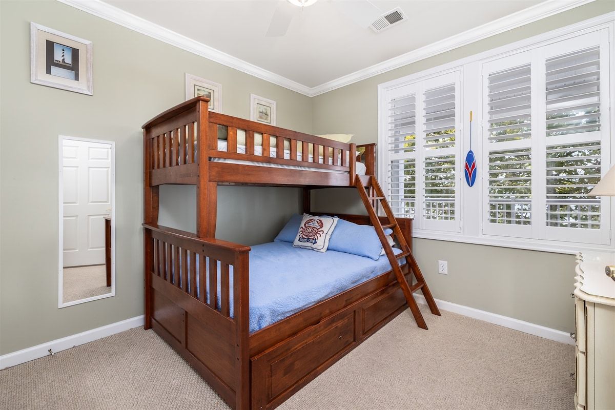 Una cama litera con escalera, una ventana con contraventanas y una puerta.