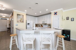 Una cocina con armarios blancos, una isla central con taburetes, un refrigerador y un microondas.
