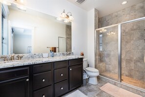 A modern bathroom with a large mirror, dark cabinetry, a shower enclosure, and a marble countertop.
