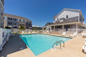 A swimming pool with lounge chairs and a covered area, surrounded by buildings with balconies.