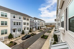 A row of townhouses with attached porches, a clear sky, and a street with parked cars.