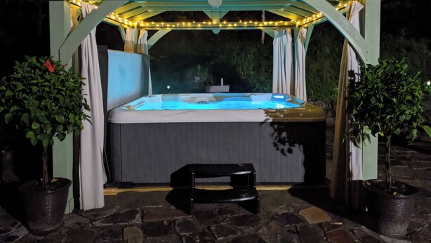 Un jacuzzi bajo un porche con luces de cadena, rodeado de plantas en macetas.