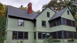 Una casa de dos pisos con fachada verde y detalles oscuros alrededor de las ventanas y el techo.