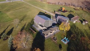 Vue aérienne d’une propriété résidentielle comprenant une grande maison, un garage séparé et une cour clôturée avec une balançoire.