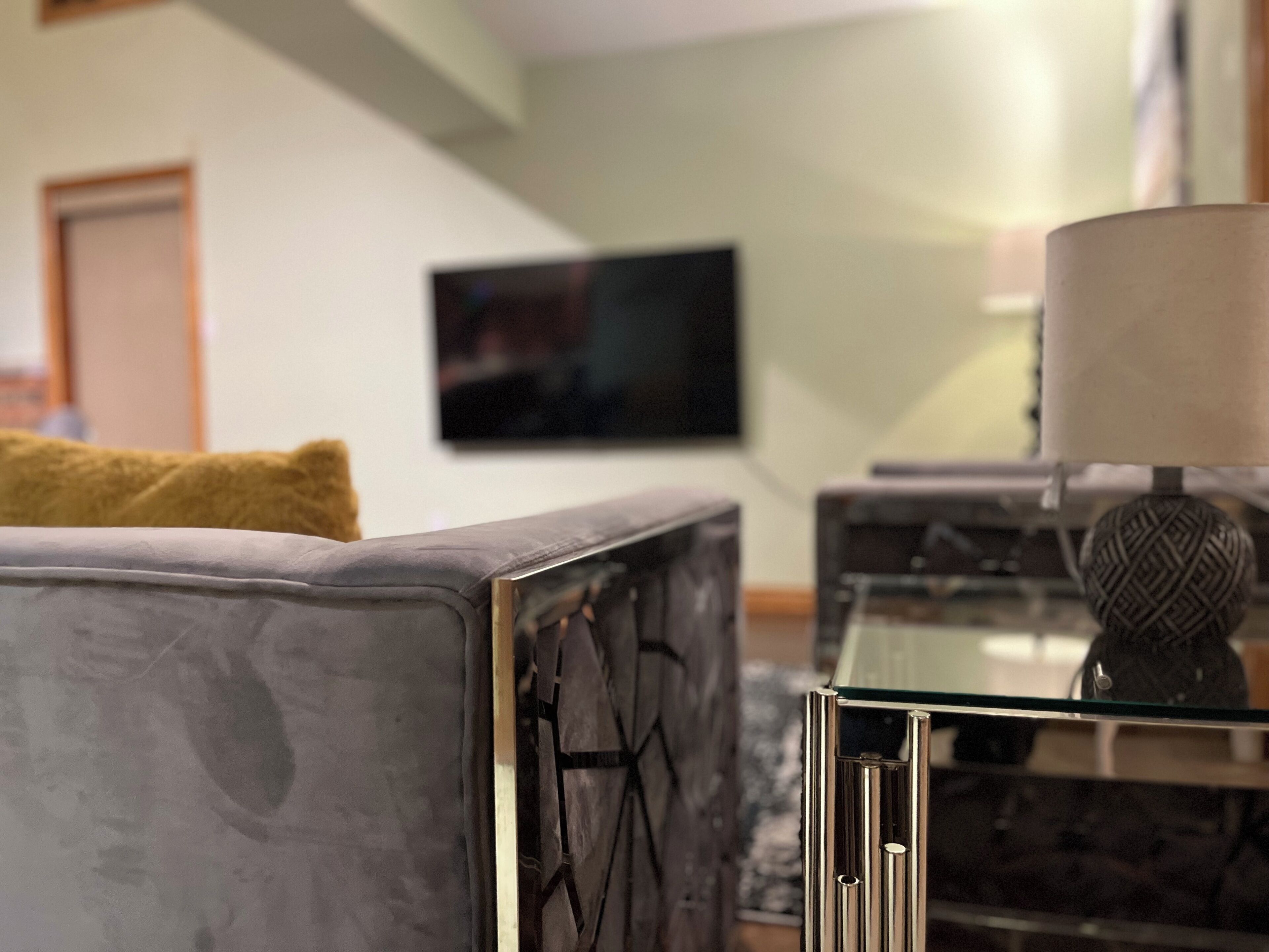 Uma sala de estar moderna com um sofá cinzento, uma mesa de centro de vidro e uma televisão fixada na parede.