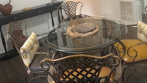 A dining area with a glass table surrounded by wicker chairs, a black metal chair, and a yellow cushioned bench.