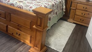A wooden bed with a floral bedspread, two side tables, a nightstand, and a framed picture on the wall.