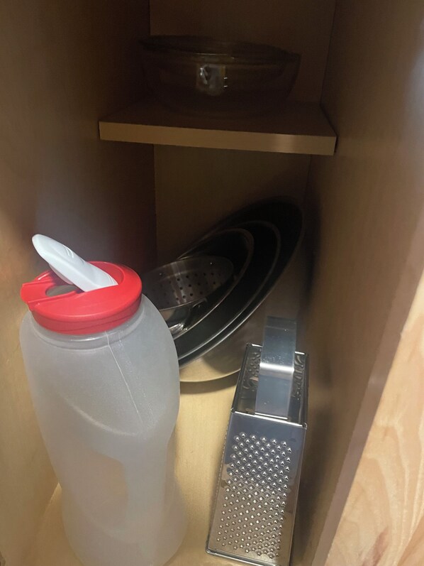 A kitchen with a large plastic container, a colander, and a grater.