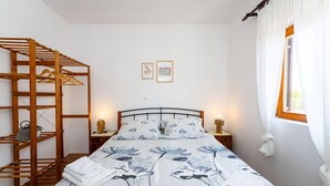 A bedroom with a bed, wooden shelving unit, two bedside tables with lamps, and a window with curtains. - Awesome home in Murvica Gornja (Murvica Gornja)