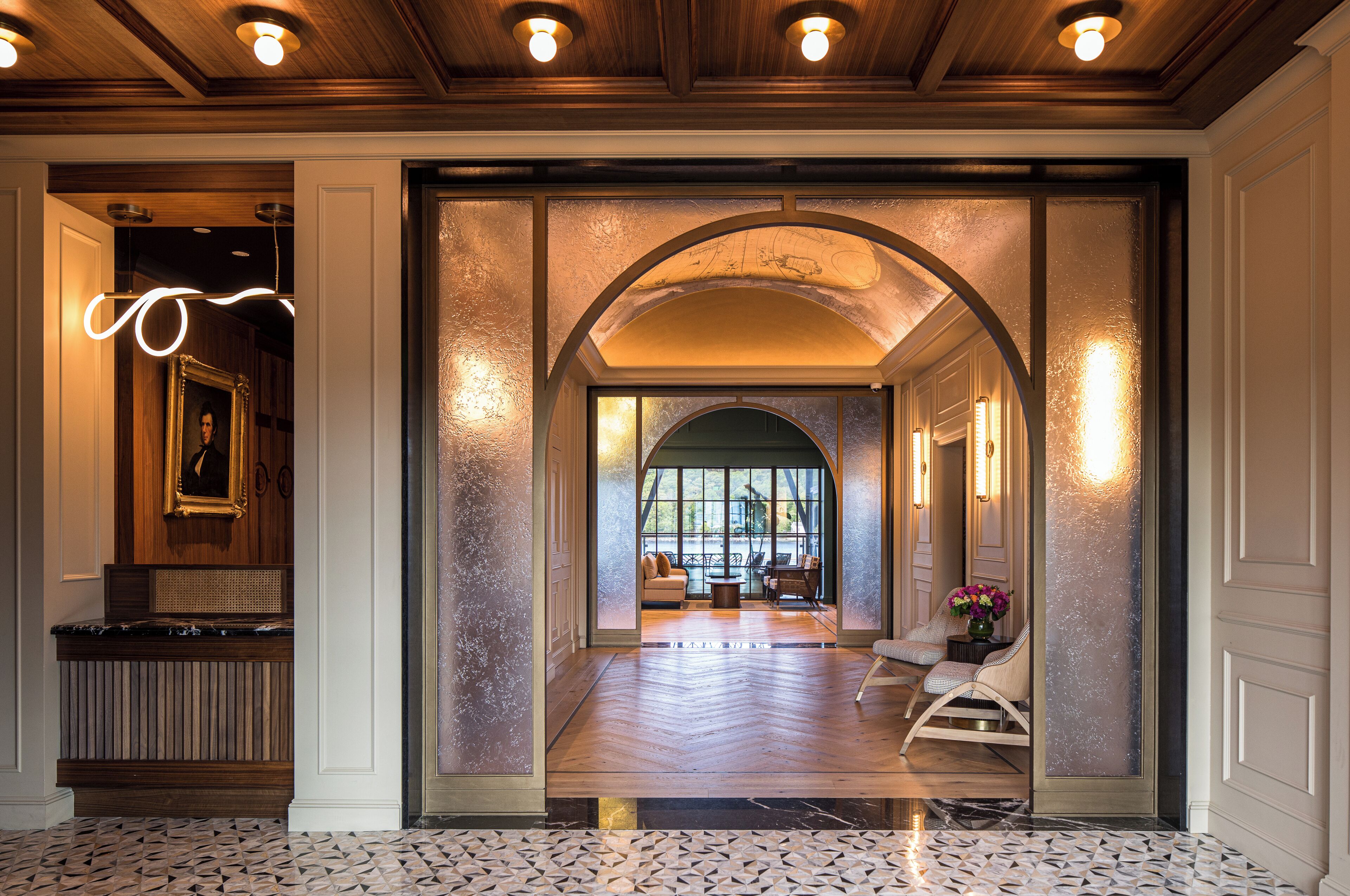 Un hall d’hôtel avec un comptoir d’accueil en bois, un grand miroir et un espace détente comprenant des chaises et une table.