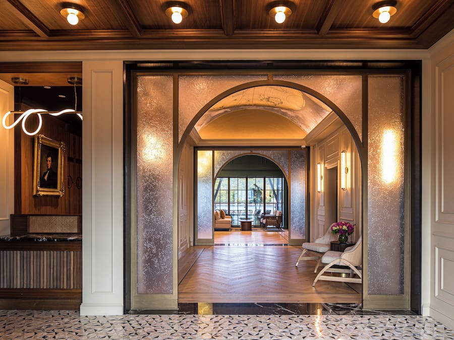 A hotel lobby with a wooden reception desk, a large mirror, and a seating area with chairs and a table.