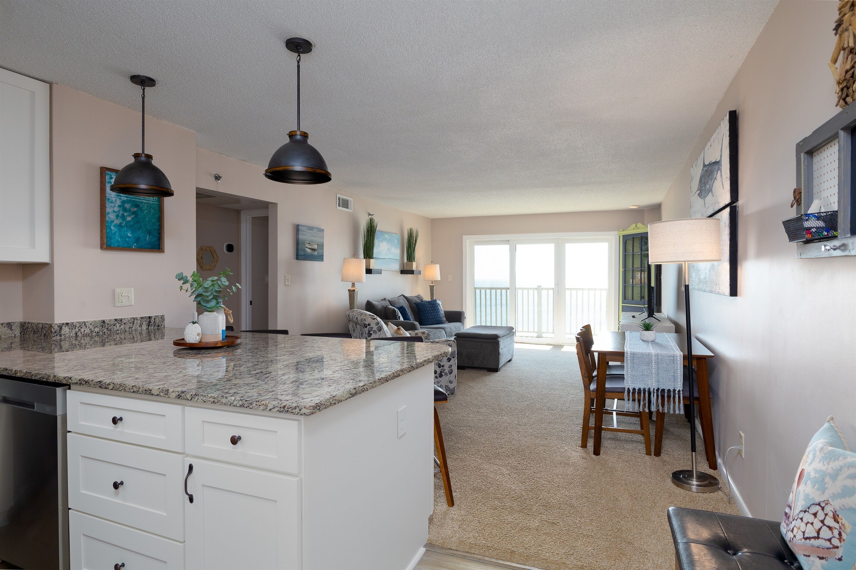 A modern kitchen with granite countertops, white cabinetry, and pendant lighting.