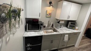 Uma cozinha moderna com armários brancos, geladeira preta, micro-ondas e pia.