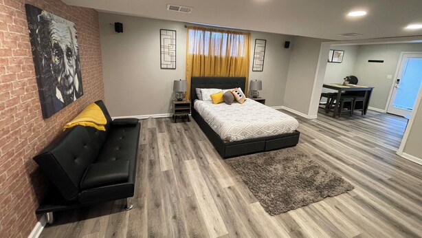 Um quarto moderno com cama, sofá preto, escrivaninha e espaço para refeições.