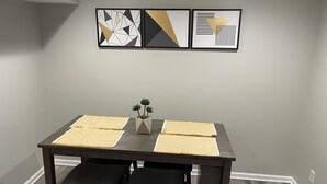 Uma mesa de jantar com duas cadeiras, uma pequena planta e três obras de arte emolduradas na parede.