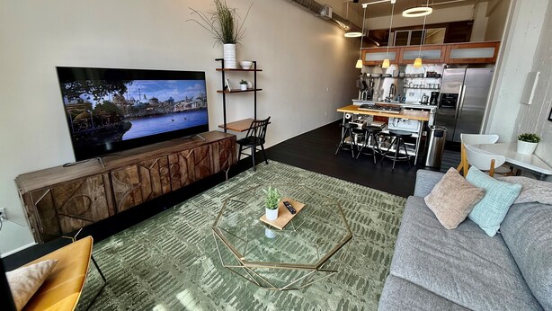 A modern living room with a flat-screen TV, a sofa, a coffee table, and a kitchen area with a dining set.