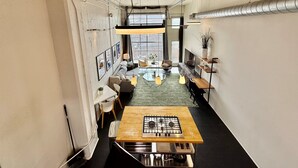 A narrow, well-lit kitchen with a central island, a dining area with a table and chairs, and a view through a large window.