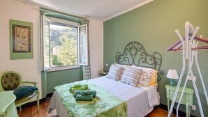 A bedroom with a bed, a window with a view of trees and buildings, a green chair, and a small table with a lamp. - Pet friendly apartment in Sori with WiFi (Sori)