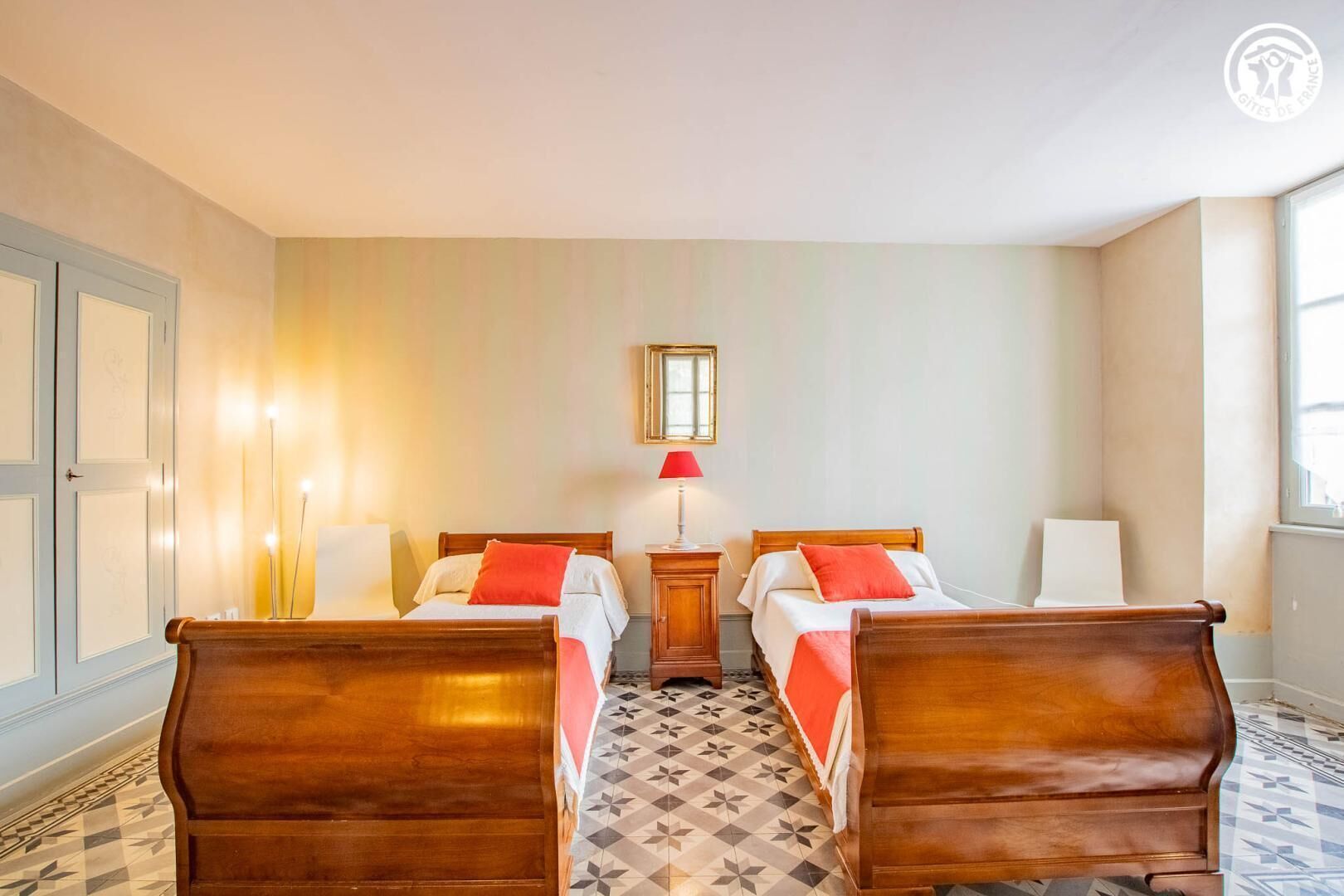 A hotel room with two wooden beds, a small table, a mirror, and a window.