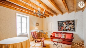 A cozy living room with a wooden ceiling, a red sofa, a rocking chair, a small table, and a large window. - Auprès de mon arbre - PLOTTES (PLOTTES)